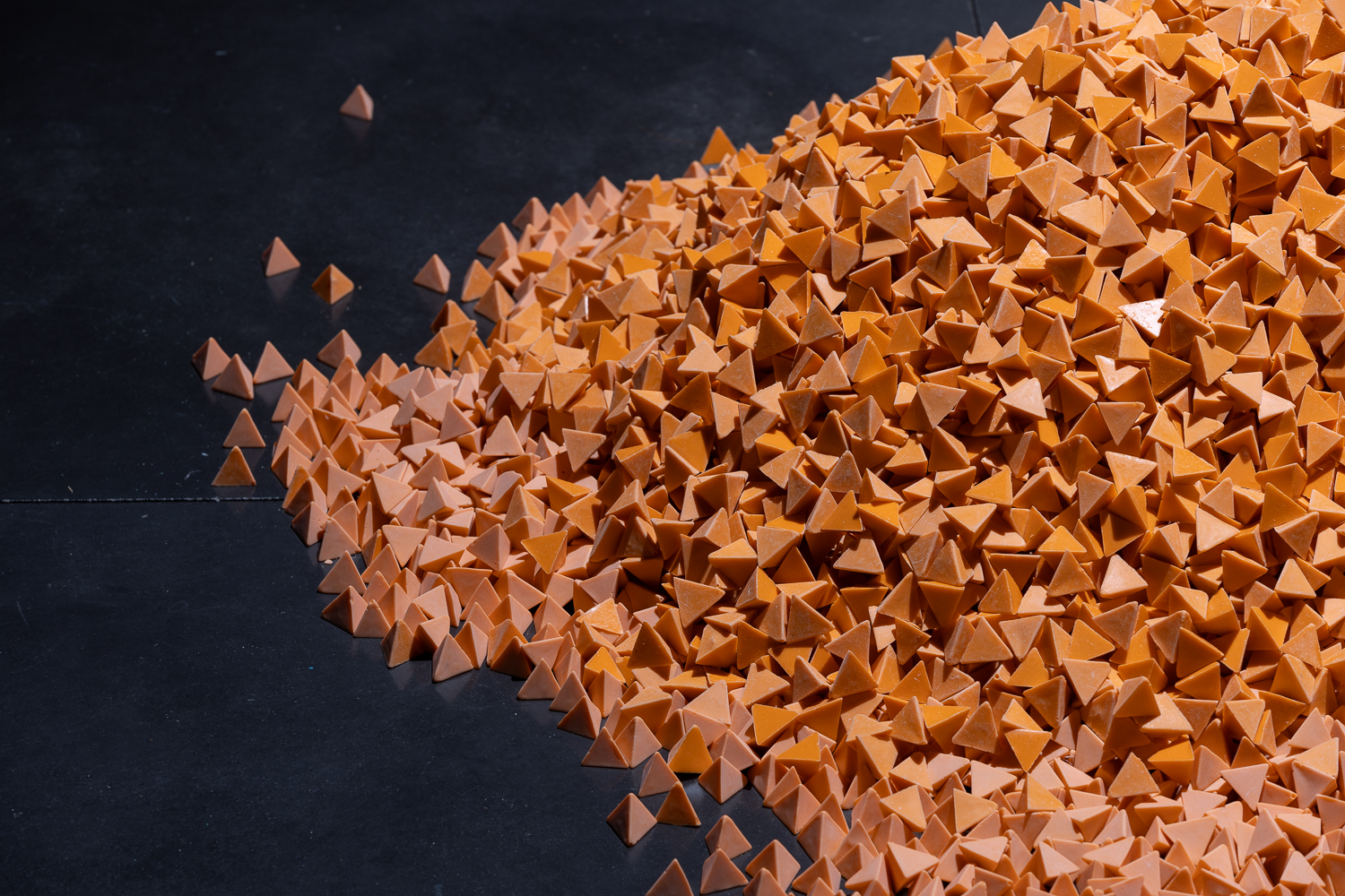 A pile of bright orange material on a black floor. Each piece of the material is a small pyramid shape.
