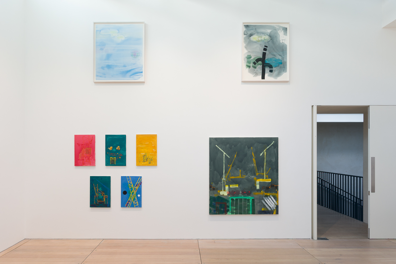 A white walled gallery with colourful abstract paintings hanging at varying heights on the wall.