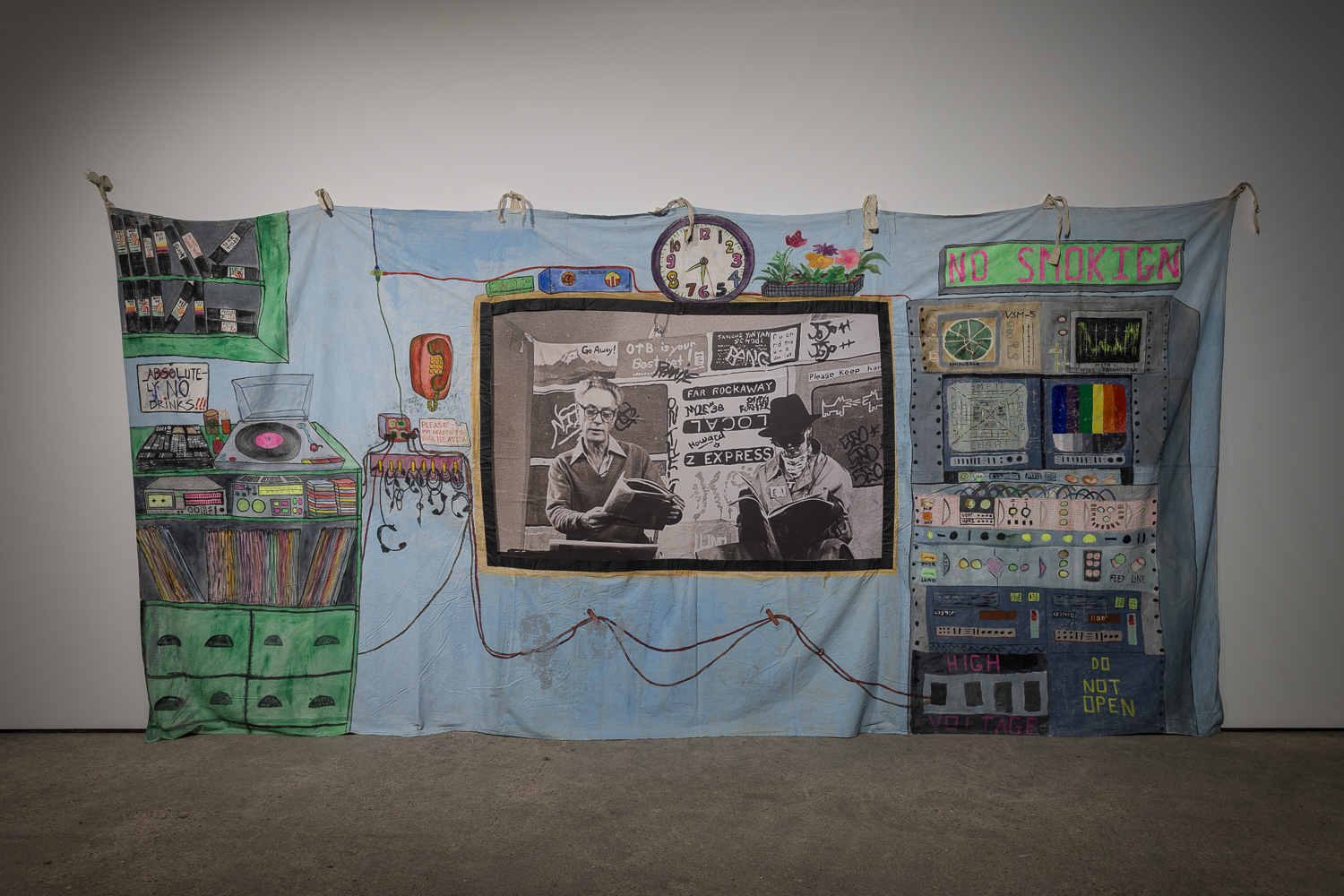 A colourful hand painted backdrop depicting a television control room hangs on a white wall.