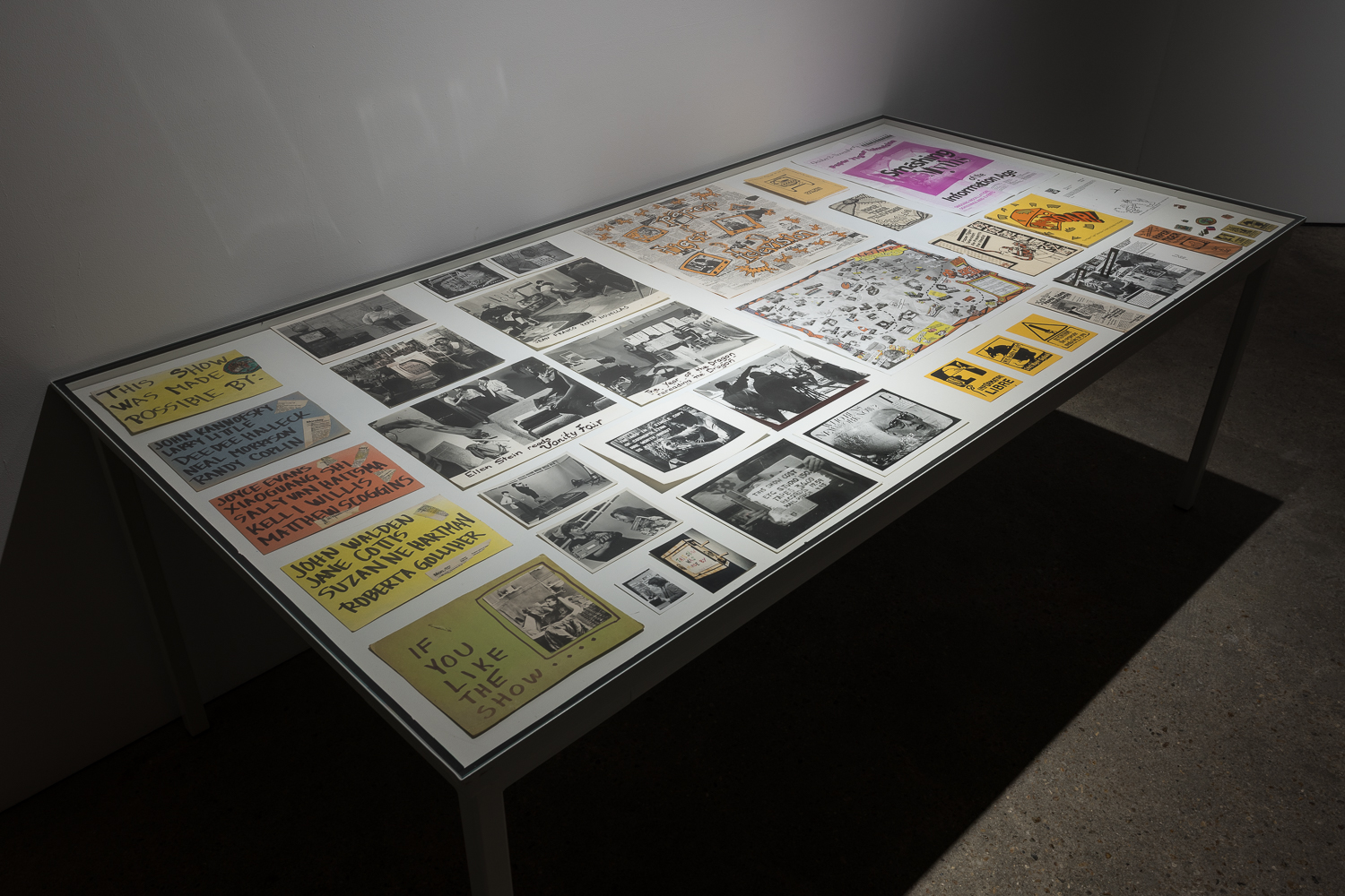 A large vitrine containing hand Witten credit cards on colourful paper, black and white photographs, and Paper Tiger Television paper material and merchandise.