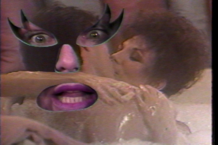 Television still of a man and a woman kissing in a bubble bath. The image has cut outs for eyes, nose, and mouth, behind which is the wide eyed and open-mouthed face of Joan Braderman.