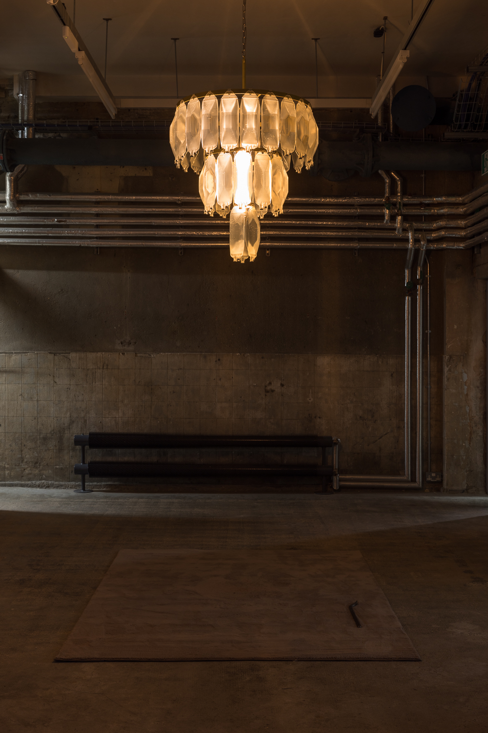 a chandelier-like structure hanging from the ceiling of an industrial-style building. The structure is made up of what looks like IV drip bags.