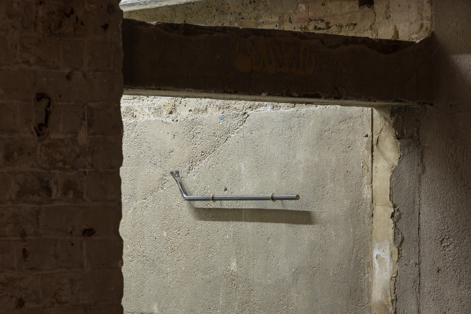 a metal crowbar is installed neatly and horizontally on a concrete wall behind a doorway.
