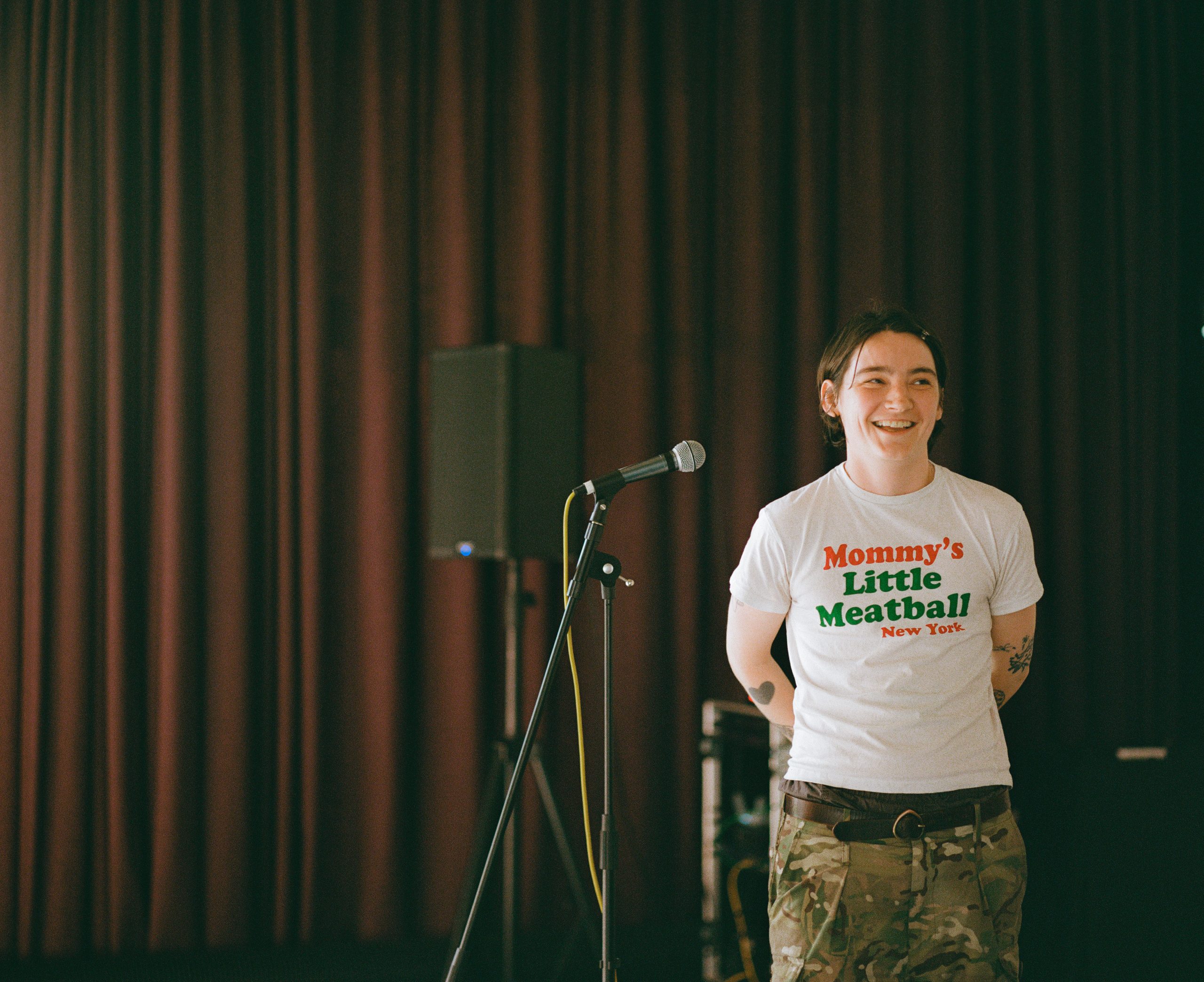 Someone standing in front of a purple curtain next to a microphone.