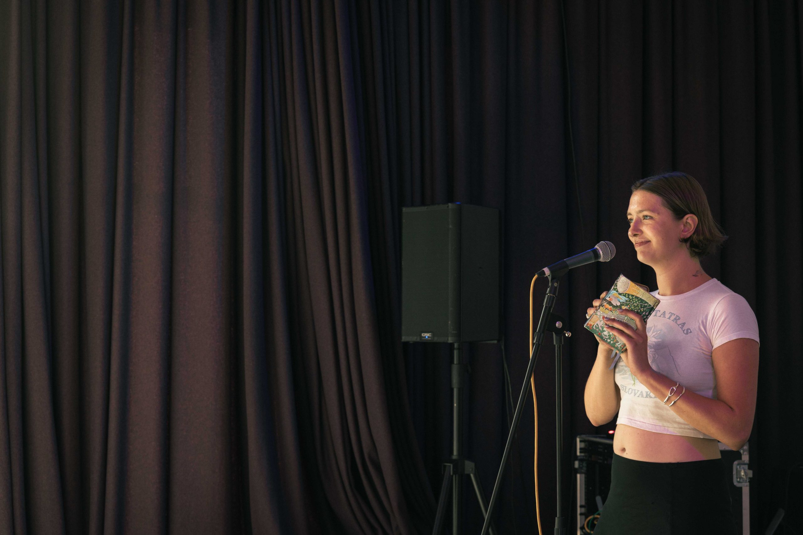a person talking into a microphone, standing in front of a purple curtain.