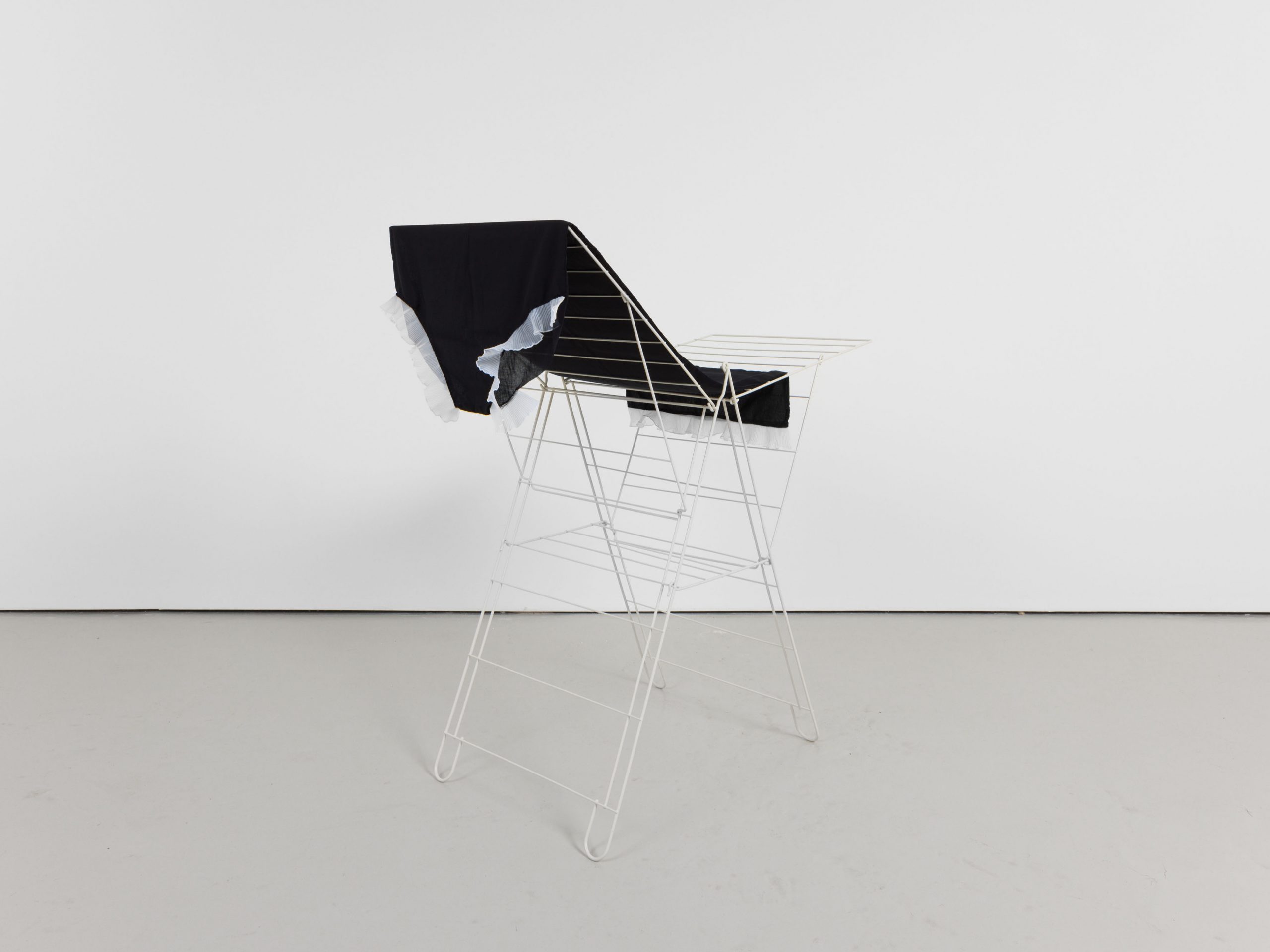 A white metal clothes drying rack with a pair of exaggeratedly oversized black underwear draped over one side, set against a plain white background.