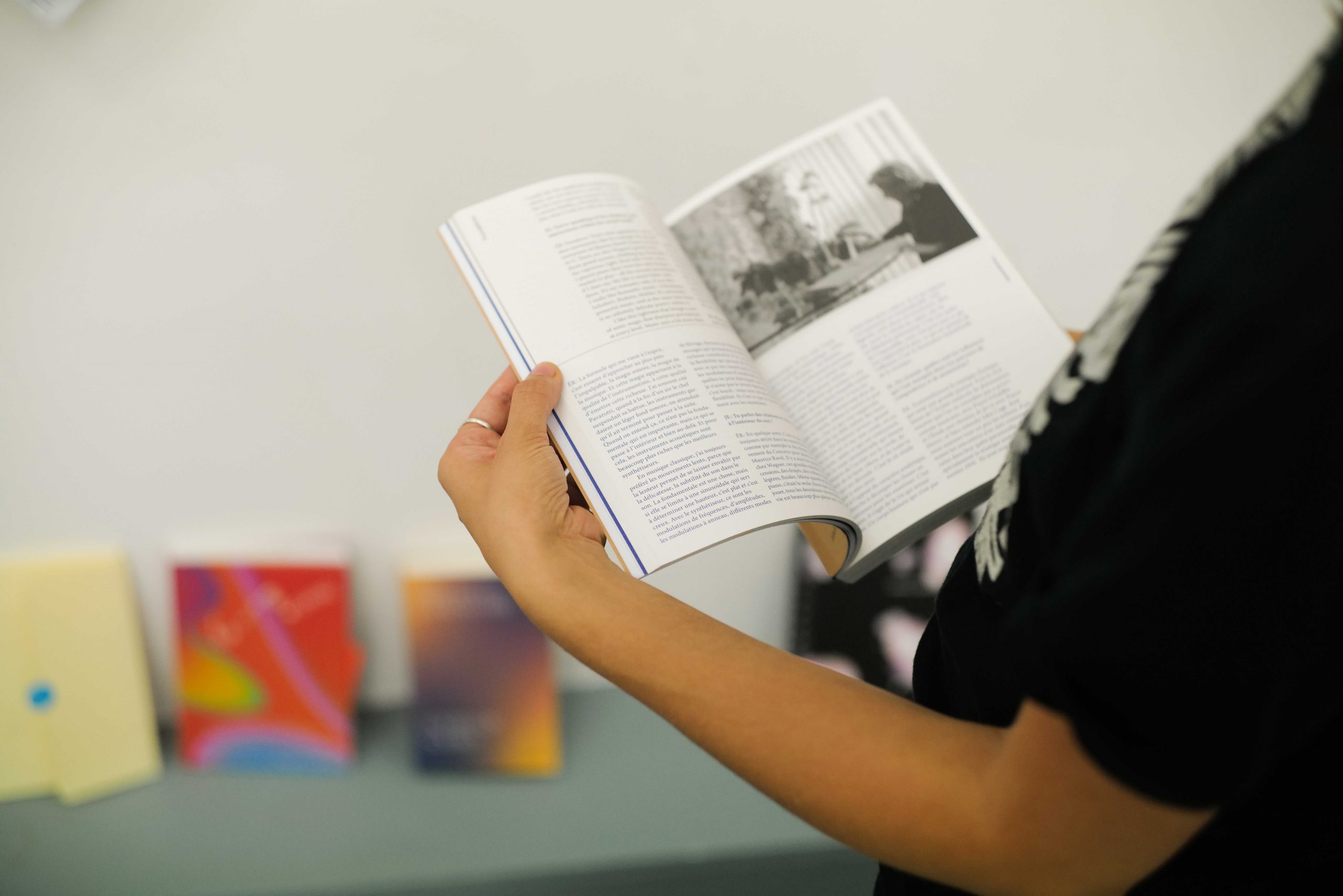 A person holds a book open with text and a black and white image in the top right page.