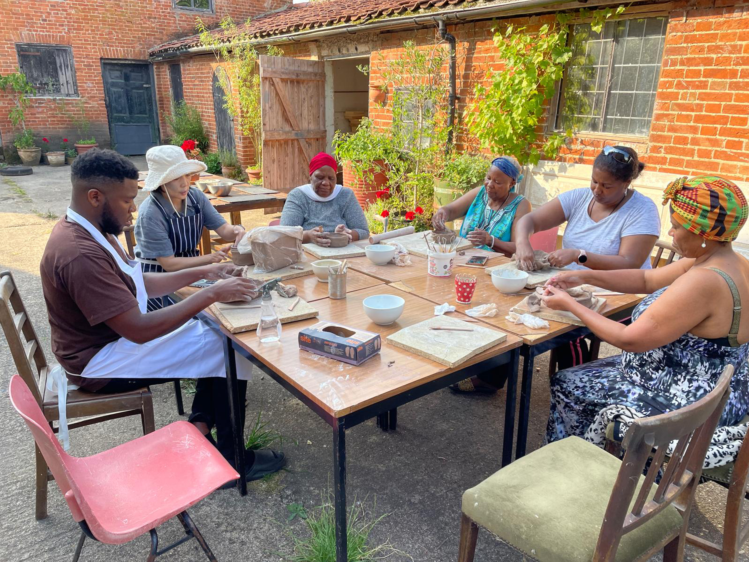 A group of people sit around a table outside. They are engaged in a creative activity.